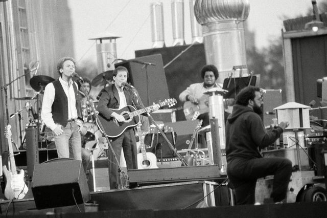 Paul Simon and Art Garfunkel perform in Central Park, black and white photograph, on a stage with band members